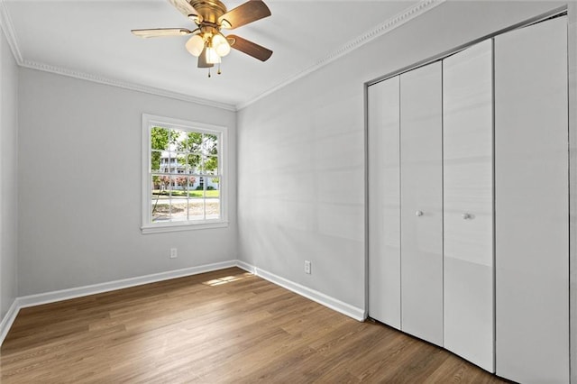 unfurnished bedroom featuring baseboards, ornamental molding, wood finished floors, and a closet
