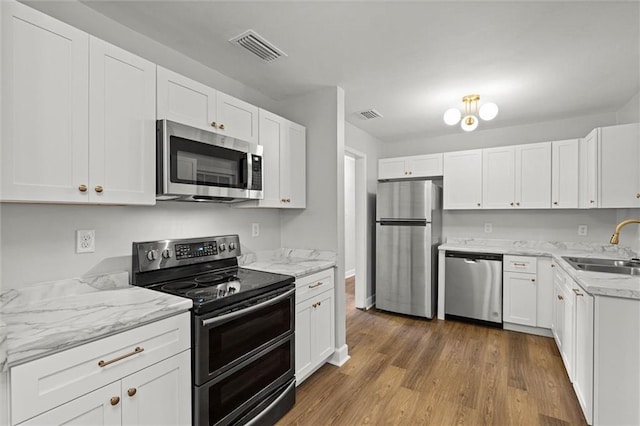 kitchen featuring visible vents, appliances with stainless steel finishes, wood finished floors, a sink, and white cabinetry