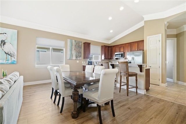 dining area with lofted ceiling, light wood-type flooring, baseboards, and crown molding