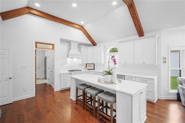 kitchen featuring a kitchen island, lofted ceiling with beams, white cabinetry, and wall chimney range hood