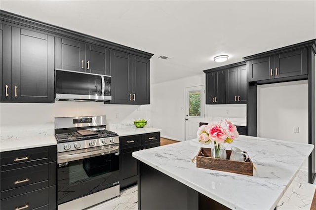 3510 Zimlich Ave, Mobile, AL 36608 - kitchen featuring appliances with stainless steel finishes, dark cabinets, light marble finish floors, a center island, and light stone countertops
