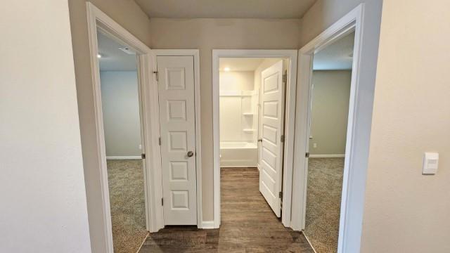 corridor featuring dark colored carpet and baseboards