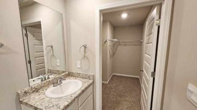 bathroom with a walk in closet, vanity, and baseboards