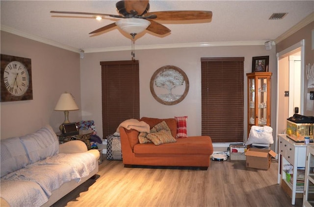 living room with light wood-style floors, visible vents, ornamental molding, and a ceiling fan