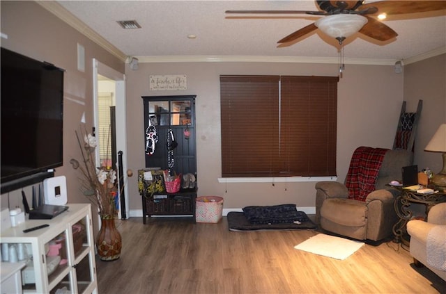 living room featuring ceiling fan, visible vents, ornamental molding, and wood finished floors