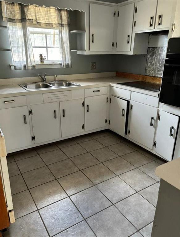 kitchen with white cabinets, black appliances, light tile patterned flooring, and sink