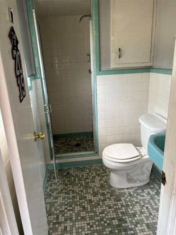 bathroom with tile walls, toilet, walk in shower, and tile patterned flooring