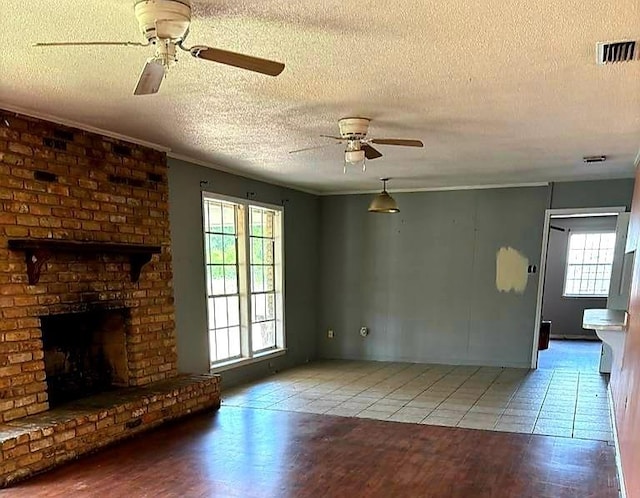 unfurnished living room with a textured ceiling, ceiling fan, a brick fireplace, and tile patterned flooring