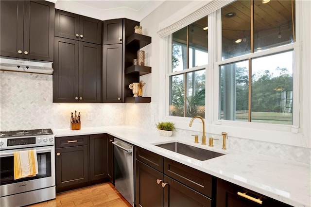 kitchen with under cabinet range hood, a sink, light wood-style floors, appliances with stainless steel finishes, and backsplash