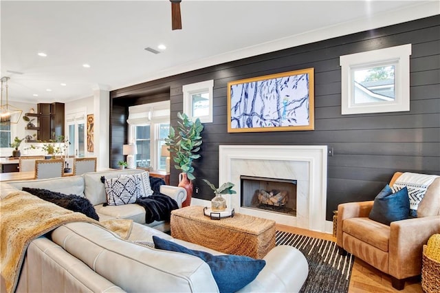 living area with recessed lighting, a premium fireplace, visible vents, light wood-style floors, and crown molding