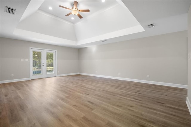 empty room featuring french doors, a tray ceiling, ceiling fan, and hardwood / wood-style floors