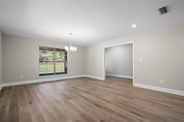 empty room featuring wood-type flooring and an inviting chandelier