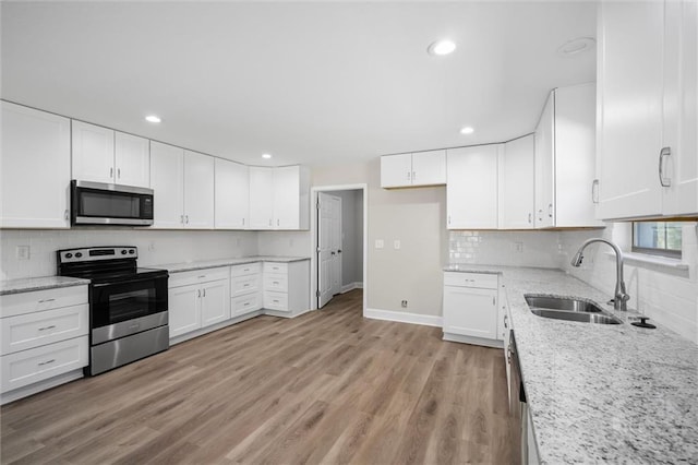 kitchen with white cabinets, sink, light wood-type flooring, appliances with stainless steel finishes, and light stone counters