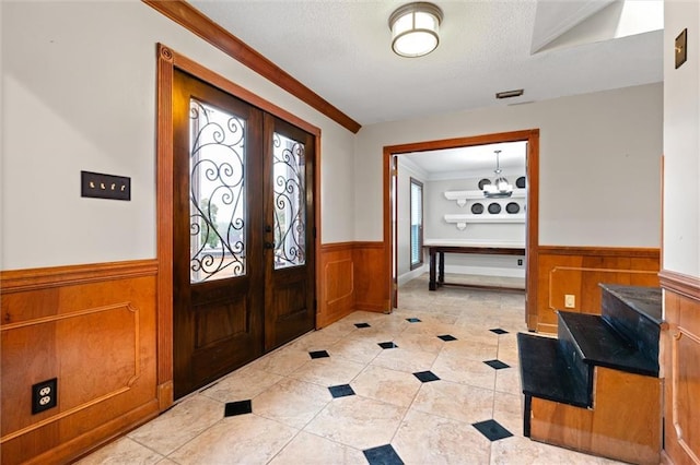 foyer entrance featuring ornamental molding, a healthy amount of sunlight, a notable chandelier, and french doors