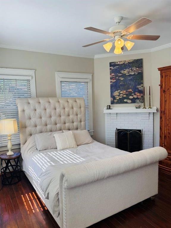 bedroom with a fireplace, crown molding, wood-type flooring, and ceiling fan