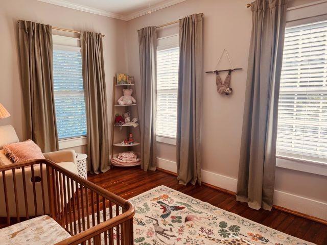 bedroom with baseboards, multiple windows, crown molding, and wood finished floors