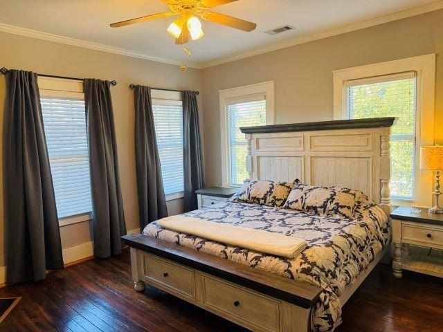bedroom with dark wood-type flooring, baseboards, visible vents, ceiling fan, and ornamental molding