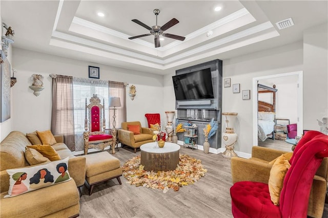 living room featuring a raised ceiling, ceiling fan, crown molding, and hardwood / wood-style flooring