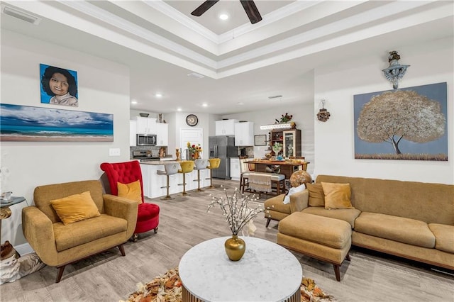 living room featuring a raised ceiling, ceiling fan, light hardwood / wood-style flooring, and ornamental molding