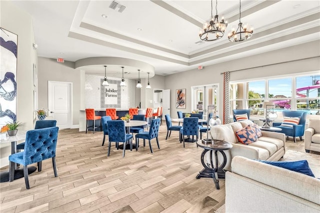 living room with light wood-type flooring, an inviting chandelier, a raised ceiling, and crown molding