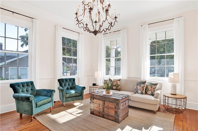 living area with wood-type flooring, a chandelier, crown molding, and baseboards