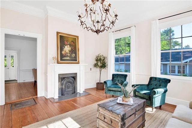 living area featuring ornamental molding, hardwood / wood-style flooring, a chandelier, a fireplace with raised hearth, and baseboards