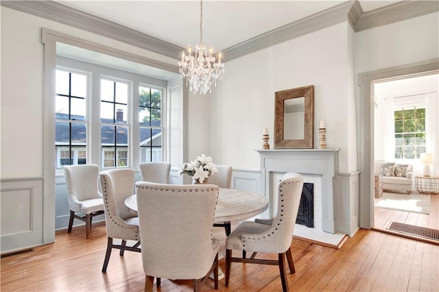 dining area with crown molding, light wood-type flooring, a chandelier, wainscoting, and a fireplace
