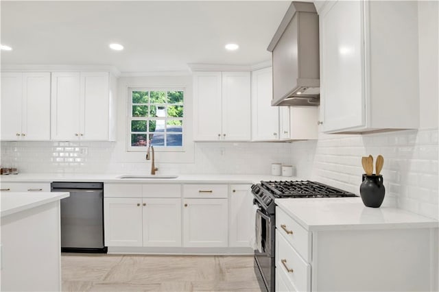 kitchen featuring appliances with stainless steel finishes, a sink, wall chimney exhaust hood, light countertops, and white cabinets