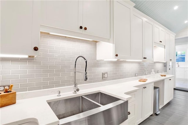 kitchen featuring a sink, white cabinetry, decorative backsplash, light countertops, and vaulted ceiling