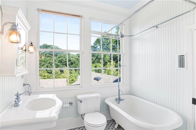 bathroom with a freestanding bath, toilet, healthy amount of natural light, and a sink