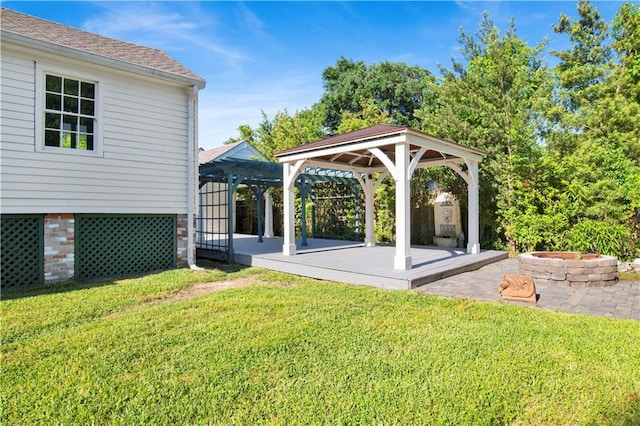 view of green lawn with a gazebo, a fire pit, a deck, and a patio area