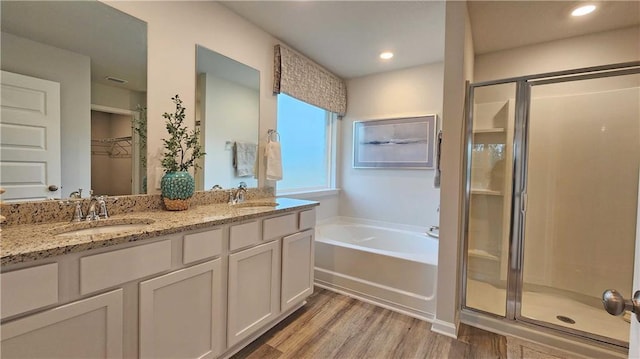 full bath featuring a spacious closet, wood finished floors, a stall shower, and a sink