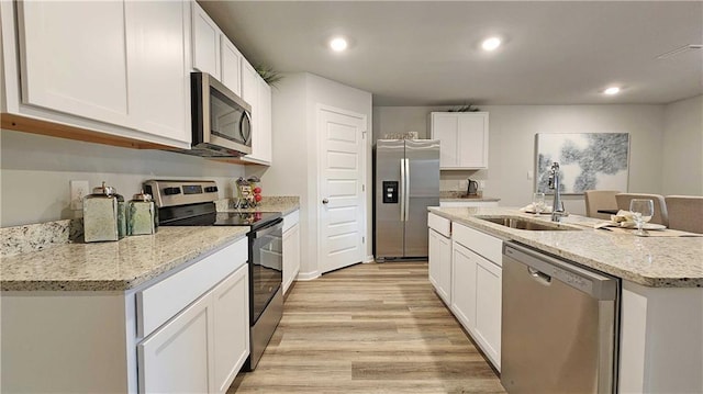 kitchen with white cabinets, an island with sink, stainless steel appliances, light wood-type flooring, and a sink