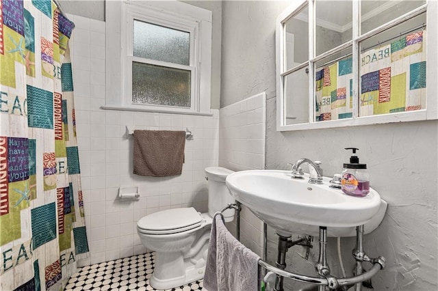 full bath featuring curtained shower, a sink, toilet, and tile walls