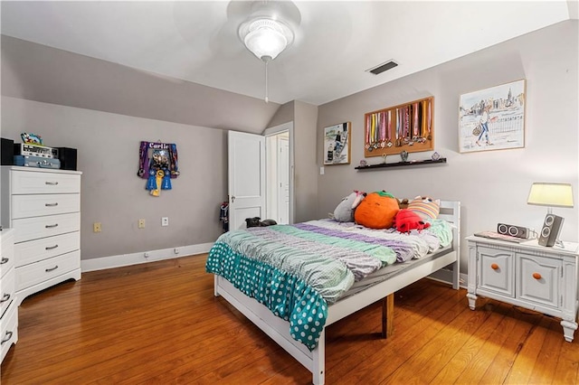 bedroom with baseboards, visible vents, vaulted ceiling, and wood finished floors