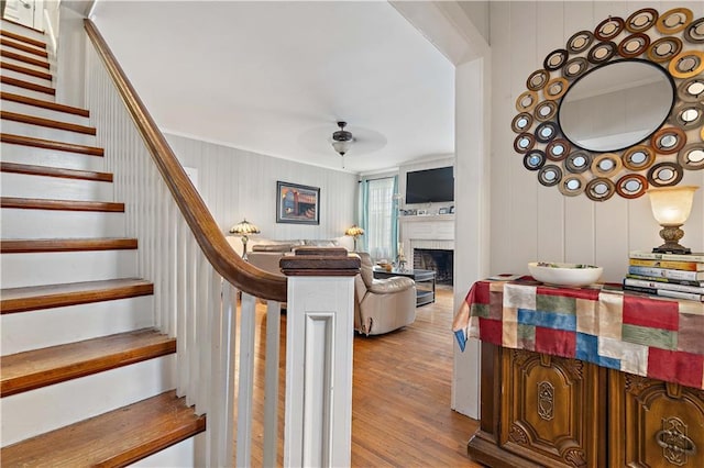 staircase featuring a fireplace, ceiling fan, and wood finished floors