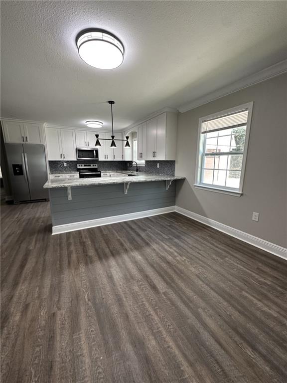 kitchen featuring kitchen peninsula, white cabinetry, dark hardwood / wood-style floors, appliances with stainless steel finishes, and pendant lighting