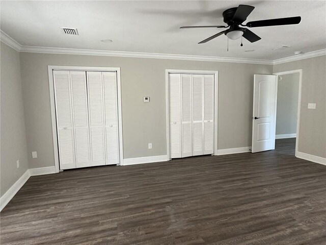 unfurnished bedroom with crown molding, two closets, ceiling fan, and dark hardwood / wood-style flooring