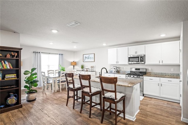 kitchen with white cabinetry, a kitchen breakfast bar, stainless steel appliances, an island with sink, and light wood-type flooring