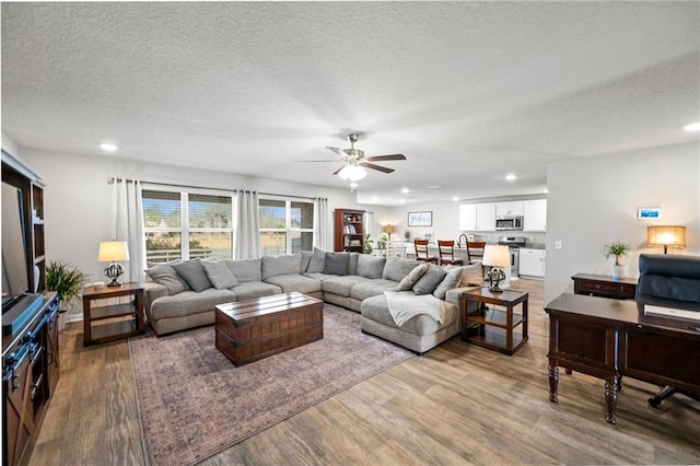 living room featuring hardwood / wood-style flooring, ceiling fan, and a textured ceiling