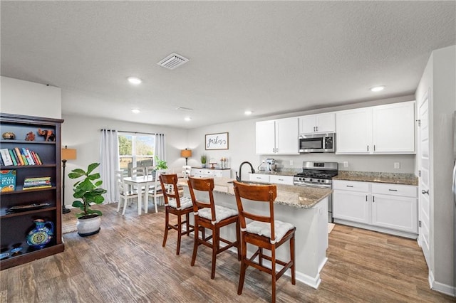 kitchen featuring a breakfast bar, light stone counters, a center island with sink, appliances with stainless steel finishes, and white cabinets