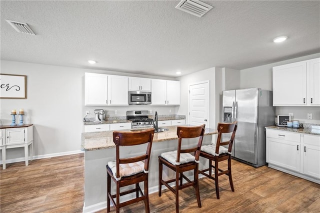 kitchen with white cabinetry, stainless steel appliances, a kitchen breakfast bar, light stone counters, and wood-type flooring