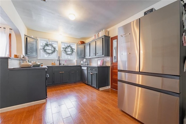 kitchen with appliances with stainless steel finishes, backsplash, light hardwood / wood-style floors, and sink