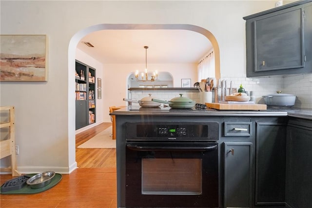 bar with pendant lighting, oven, light hardwood / wood-style flooring, decorative backsplash, and a chandelier