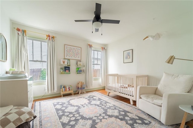 bedroom featuring multiple windows, ceiling fan, light hardwood / wood-style flooring, and a nursery area