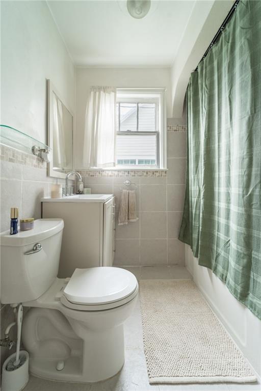 full bathroom with vanity, shower / bath combo with shower curtain, tile walls, tile patterned flooring, and toilet