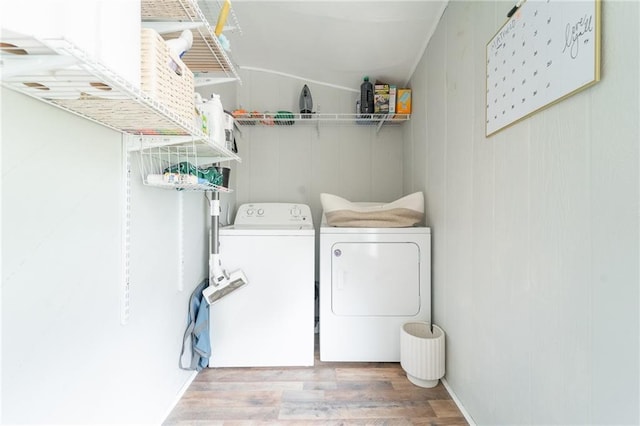 clothes washing area featuring light hardwood / wood-style floors, washing machine and dryer, and wooden walls