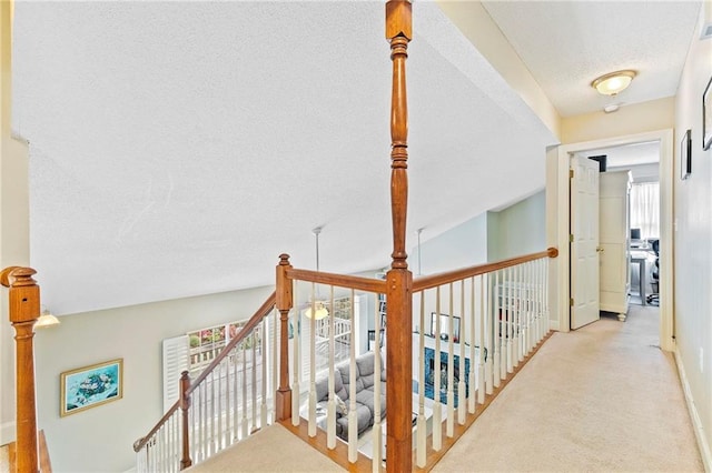 corridor with lofted ceiling, light carpet, and a textured ceiling