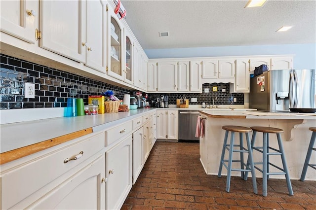 kitchen featuring a textured ceiling, backsplash, a kitchen bar, white cabinetry, and appliances with stainless steel finishes