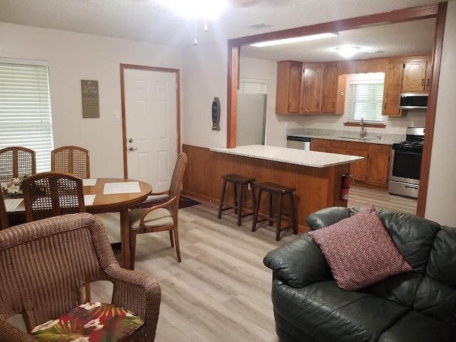 kitchen featuring sink, kitchen peninsula, light hardwood / wood-style floors, exhaust hood, and appliances with stainless steel finishes